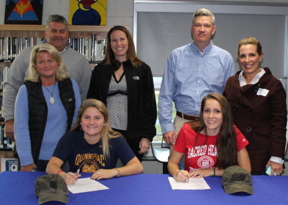 Proud parents Peter and Chrissy Cowell of Old Lyme watch as their daughter Sydney (left, seated) signs her National Letter of Intent to play lacrosse at Quinnipiac University after graduation from Lyme-Old Lyme High School. Similarly, John and Nancy Mesham of Old Lyme watch as daughter Anna (seated right) signs to play at Sacred Heart University. The girls Nor'easter club team coach (wearing black jacket) stands in the center.